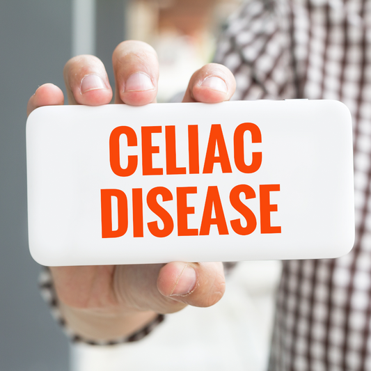 A person holds a white sign with bold orange text that reads "CELIAC DISEASE," set against a blurred background of a casual indoor environment.