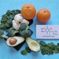 A variety of fresh foods including broccoli, cauliflower, spinach, and avocados are arranged on a light blue background, alongside two oranges and a card displaying the chemical structure of Coenzyme Q10.