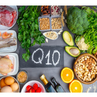A variety of foods, including vegetables, fruits, nuts, and meats, are arranged around a slate board with "Q10" written on it, highlighting sources related to CoQ10.