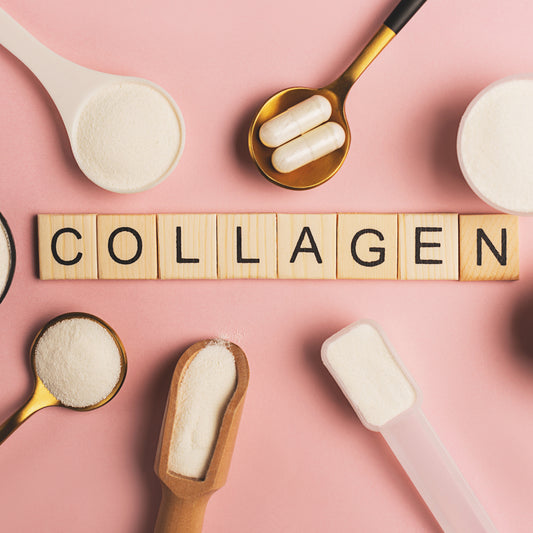 Collagen is spelled out with wooden blocks on a pink background, surrounded by various measuring spoons and scoops filled with white powder and capsules, highlighting its benefits.
