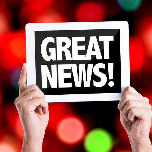 A person holds up a tablet displaying the text "GREAT NEWS!" against a blurred background of colorful lights, conveying excitement and celebration.