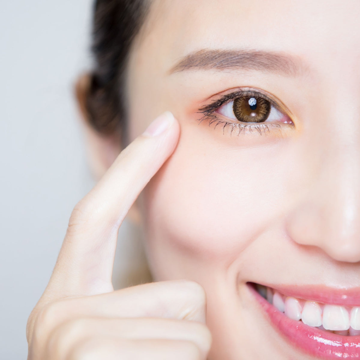 A smiling woman points to her eye, demonstrating a tip for maintaining healthy eyes, against a light gray background.