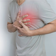 A person in a light gray shirt is holding their chest with both hands, showing signs of discomfort, against a plain white background, emphasizing the importance of heart health awareness.