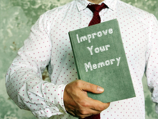 A person in a patterned shirt holds a green book titled "Improve Your Memory" against a textured, faded background, suggesting a focus on memory enhancement techniques.