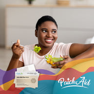 A smiling woman with short hair holds a fork with salad in one hand and a bowl of mixed vegetables in the other, sitting in a bright room with PatchAid vitamin patches visible nearby.