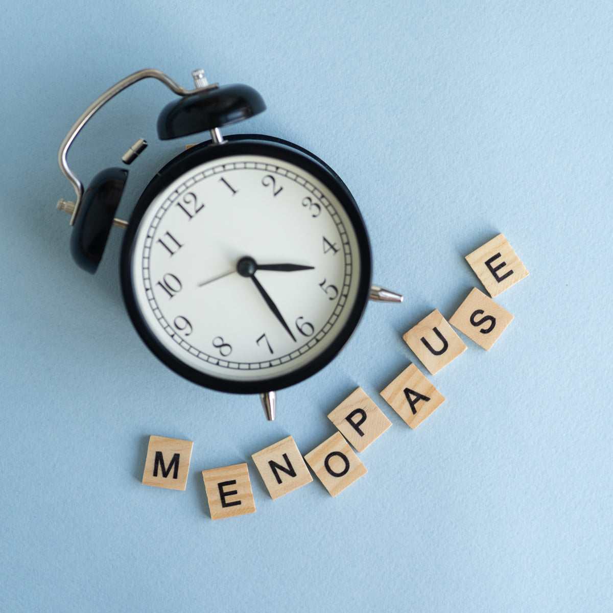 A black alarm clock sits on a light blue background next to wooden letter tiles that spell out