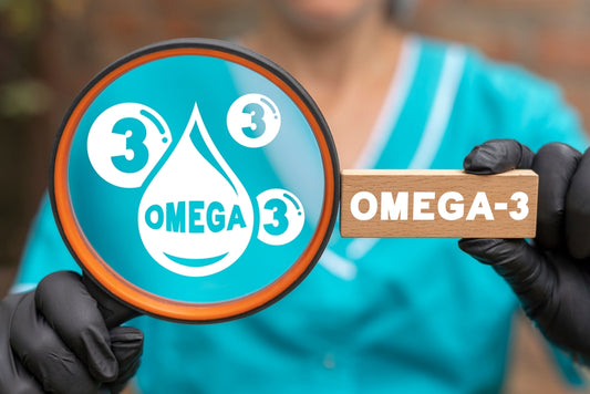 A person in a teal medical uniform holds a magnifying glass highlighting a droplet labeled "OMEGA" and the number "3," while also displaying a wooden block with "OMEGA-3" written on it.