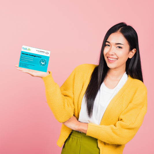 A woman in a yellow cardigan smiles while holding a box labeled "Garcinia Cambogia Patch" against a pink background, promoting vitamin patches.