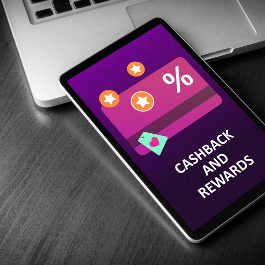 A tablet displays a colorful graphic promoting "Cashback and Rewards," featuring stars and a percentage symbol, placed on a wooden surface next to a laptop.