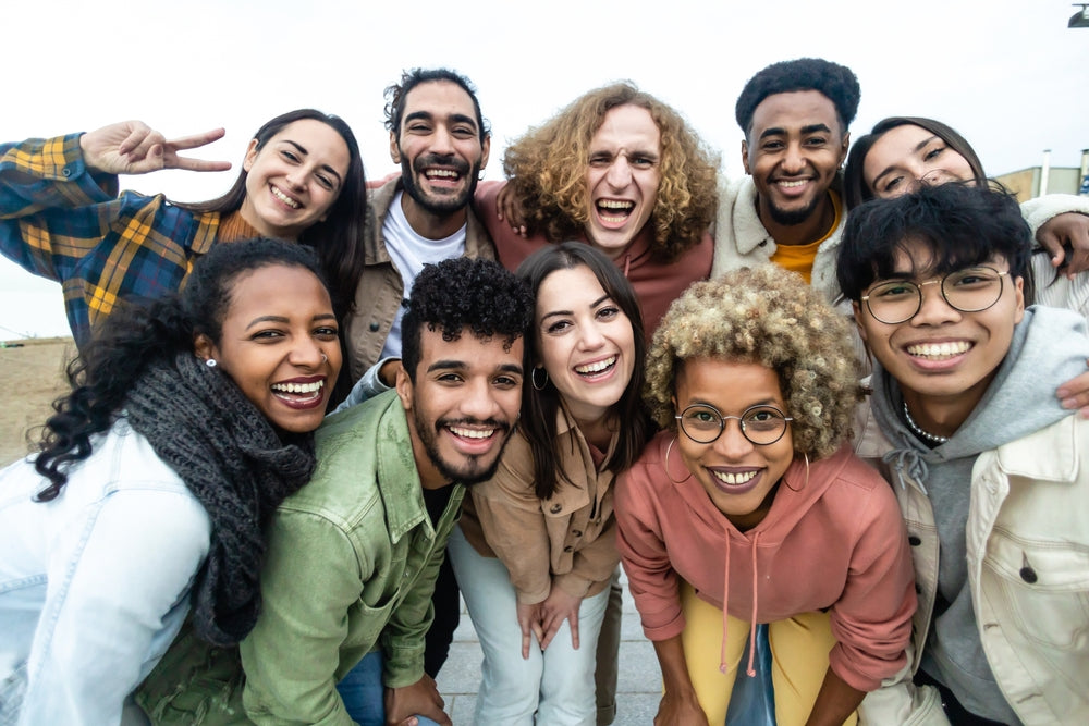 A diverse group of ten smiling young adults pose together outdoors, expressing joy and camaraderie, highlighting community and connection in relation to nutrition and well-being.