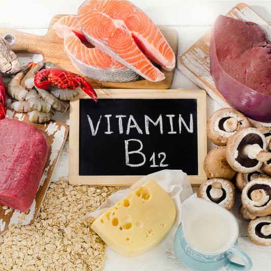 Various foods rich in Vitamin B12, including salmon, shrimp, beef, cheese, mushrooms, and oats, are arranged around a chalkboard labeled "Vitamin B12" on a light background.