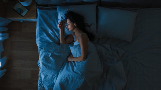 A woman sleeps peacefully in a cozy bed, surrounded by soft pillows and blankets, with dim lighting creating a calm atmosphere that emphasizes the importance of restful sleep.