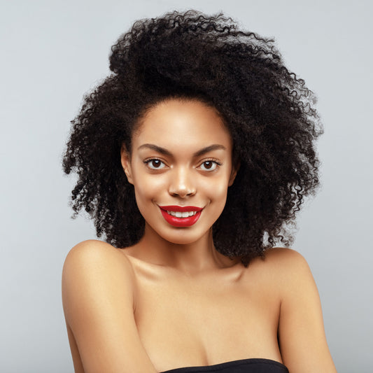 A smiling woman with curly hair and bright red lipstick poses against a light gray background, promoting confidence in hair growth and thickness through vitamin patches.