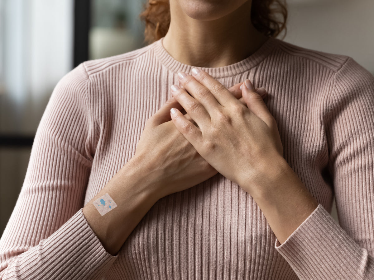 Person wearing a long-sleeve top with hands resting on their chest, showing a small square wellness patch on the wrist