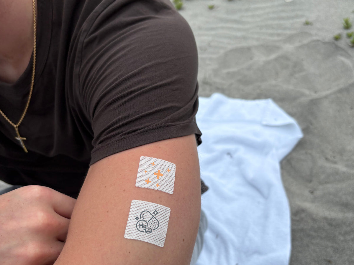Person sitting outdoors with two small square wellness patches applied to the upper arm
