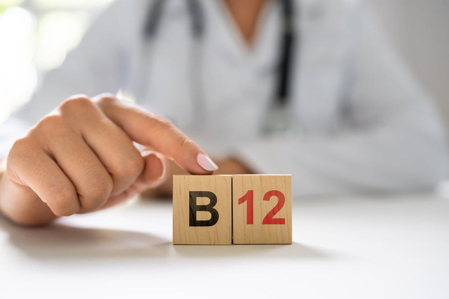 A healthcare professional's hand points to wooden blocks displaying "B" and "12," emphasizing the importance of Vitamin B12 in a bright, clinical setting.