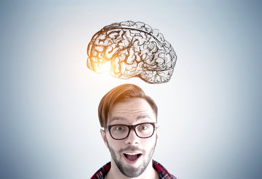 A surprised man with glasses and a plaid shirt looks up at a glowing, illustrated brain hovering above his head, symbolizing cognitive enhancement and memory improvement.