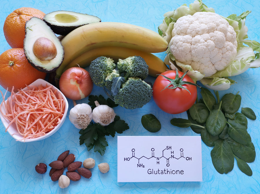 A colorful arrangement of fruits and vegetables, including oranges, avocados, bananas, broccoli, and spinach, is displayed alongside a card labeled "Glutathione" featuring its molecular structure.