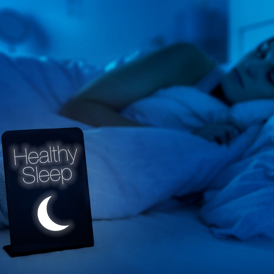 A woman sleeps peacefully in a dimly lit bedroom, while a glowing sign nearby reads "Healthy Sleep" with a crescent moon, emphasizing the importance of restful sleep.