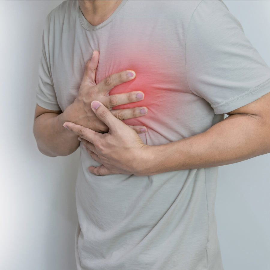 A person in a light gray shirt is holding their chest with both hands, showing signs of discomfort, against a plain white background, emphasizing the importance of heart health awareness.