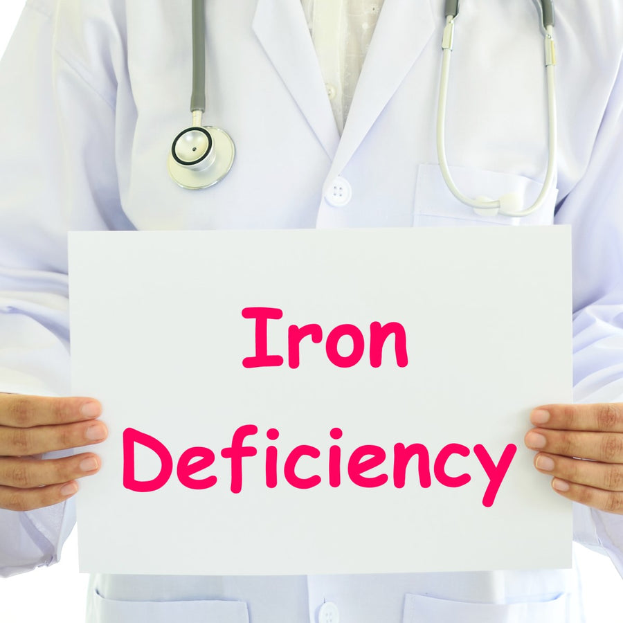 A healthcare professional in a white coat holds a sign that reads "Iron Deficiency" in bold pink letters, indicating a focus on health awareness.