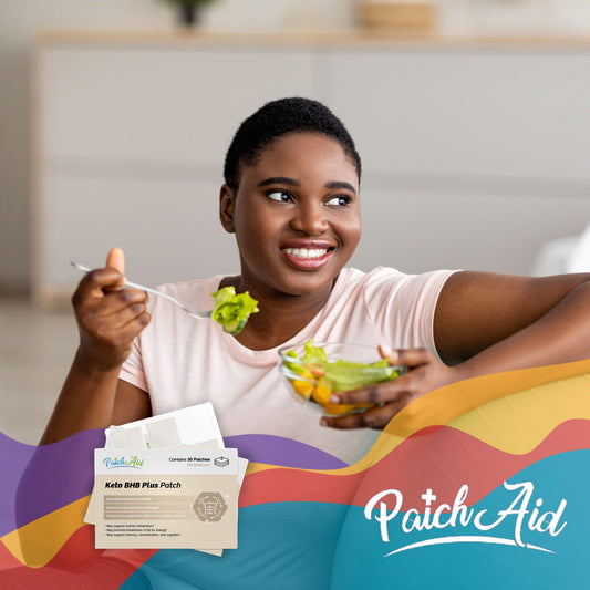 A smiling woman with short hair holds a fork with salad in one hand and a bowl of mixed vegetables in the other, sitting in a bright room with PatchAid vitamin patches visible nearby.