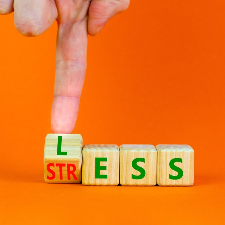 A hand is pressing down on a wooden block labeled "L," which is part of the word "STRESS," against a bright orange background, emphasizing the theme of reducing stress.