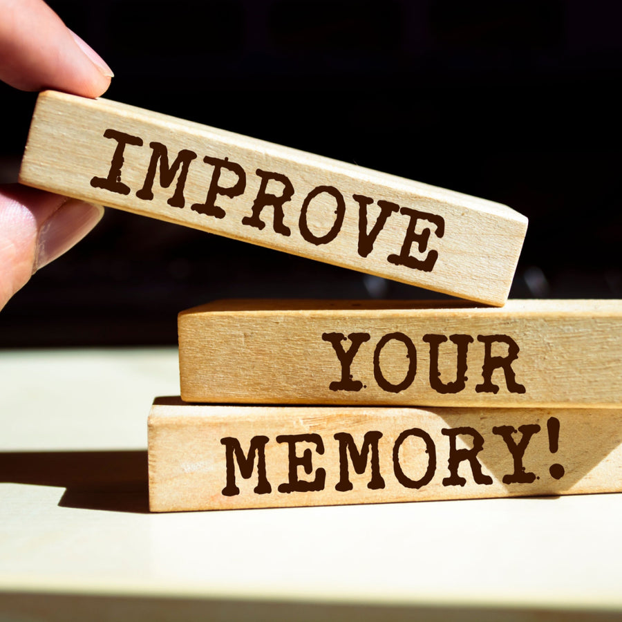 A hand holds a wooden block labeled "IMPROVE," positioned above two stacked blocks that read "YOUR MEMORY!" in a bright, well-lit setting.