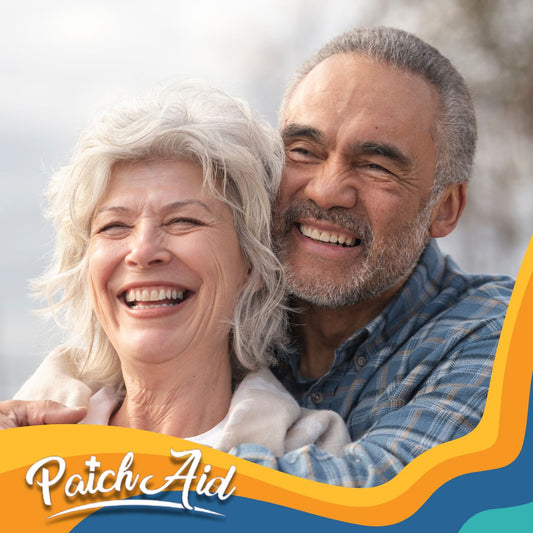 A smiling older woman and man embrace joyfully outdoors, with the woman wearing a light sweater and the man in a plaid shirt, conveying warmth and companionship, alongside the "PatchAid" logo.