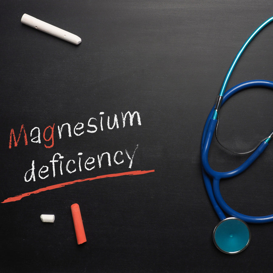 A black chalkboard displays the words "Magnesium deficiency," with the word "Magnesium" highlighted in red, alongside pieces of chalk and a blue stethoscope resting on the surface.
