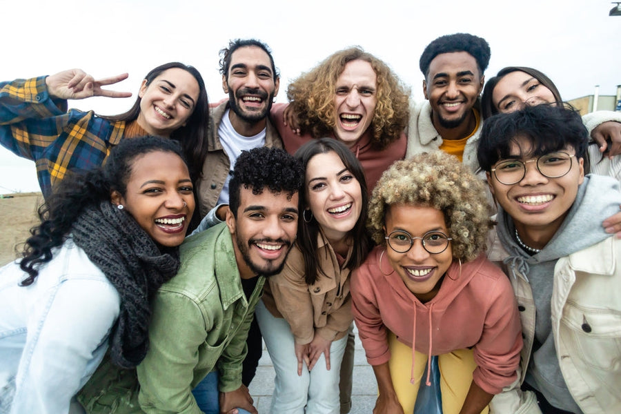 A diverse group of ten smiling young adults pose together outdoors, expressing joy and camaraderie, highlighting community and connection in relation to nutrition and well-being.