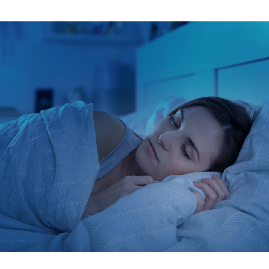 A woman peacefully sleeps in a dimly lit bedroom, wrapped in a light blanket, with her head resting on a pillow, suggesting a calm and restful environment for better sleep.