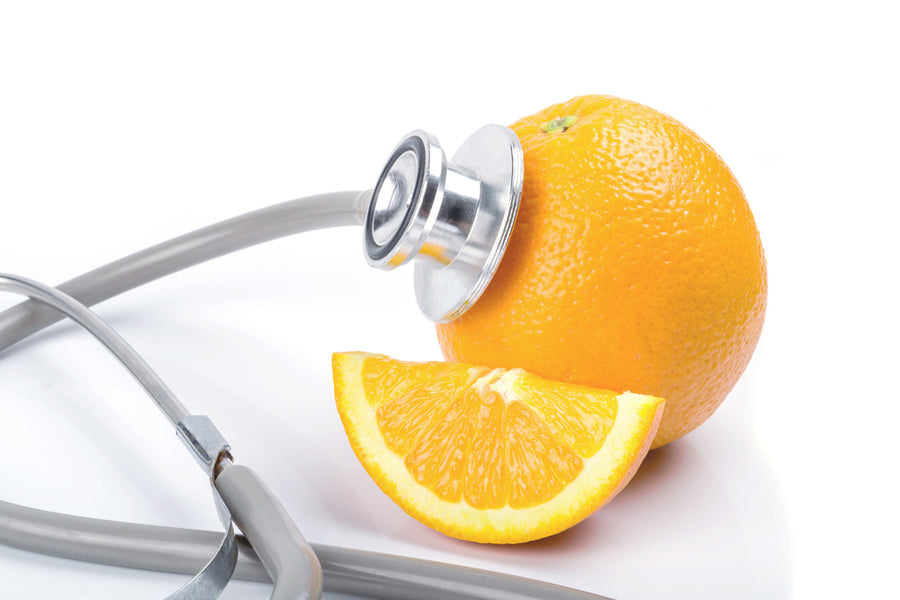 An orange and a slice are placed next to a stethoscope, symbolizing the connection between vitamin C and health.
