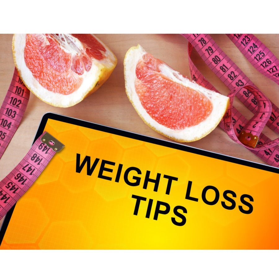 A tablet displaying "WEIGHT LOSS TIPS" sits on a wooden surface next to two halved grapefruits and a pink measuring tape, suggesting a focus on health and fitness.