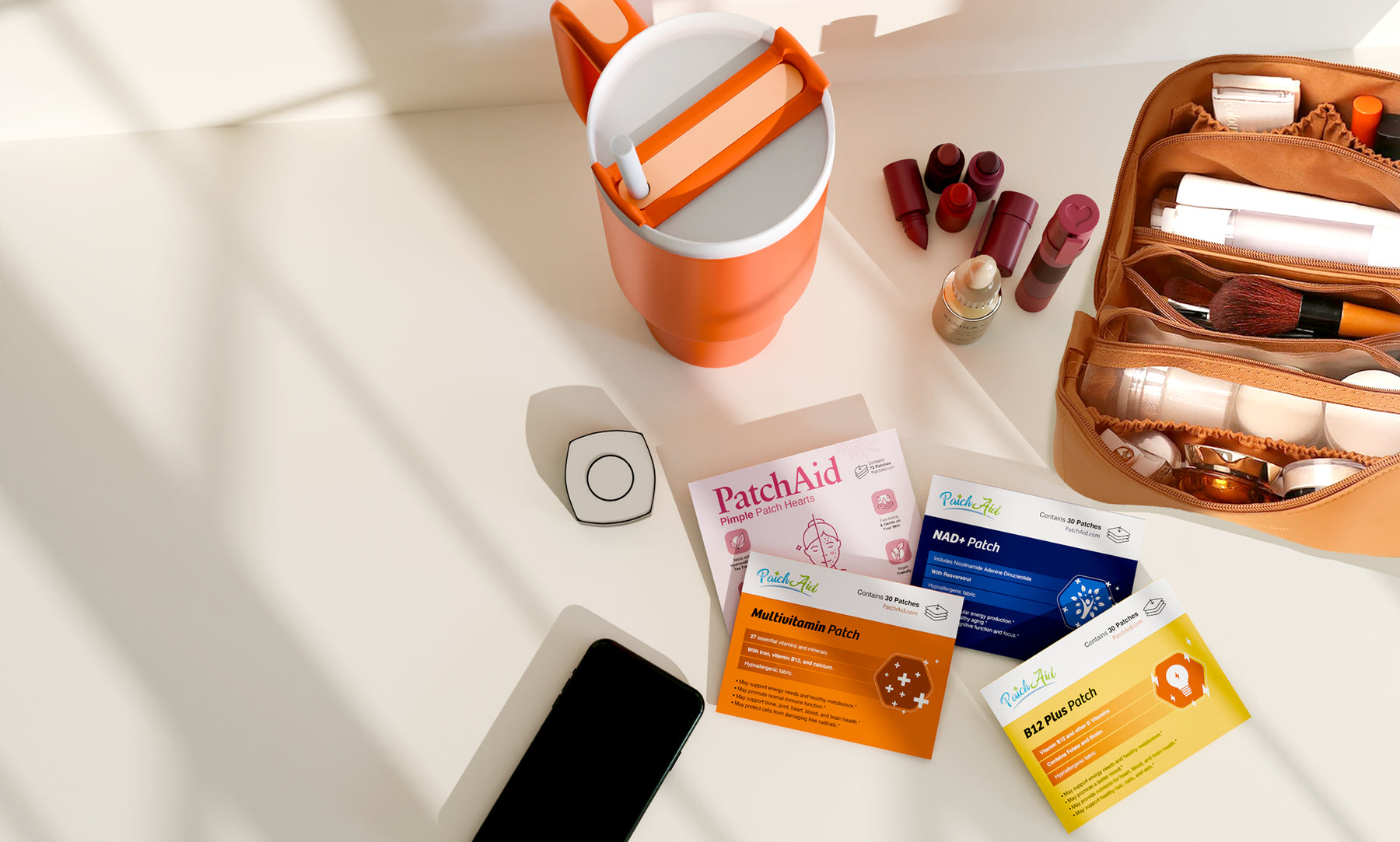 A bright orange container sits on a light surface alongside skincare patches labeled "PatchAid," a smartphone, and a makeup bag filled with various cosmetics.