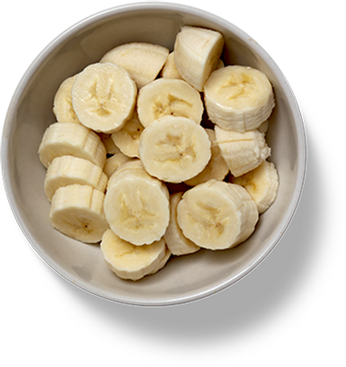 Overhead view of sliced bananas in a white bowl against a black background.